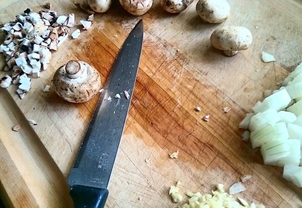 Chopping garlic and onion with a chef knife on a wooden board